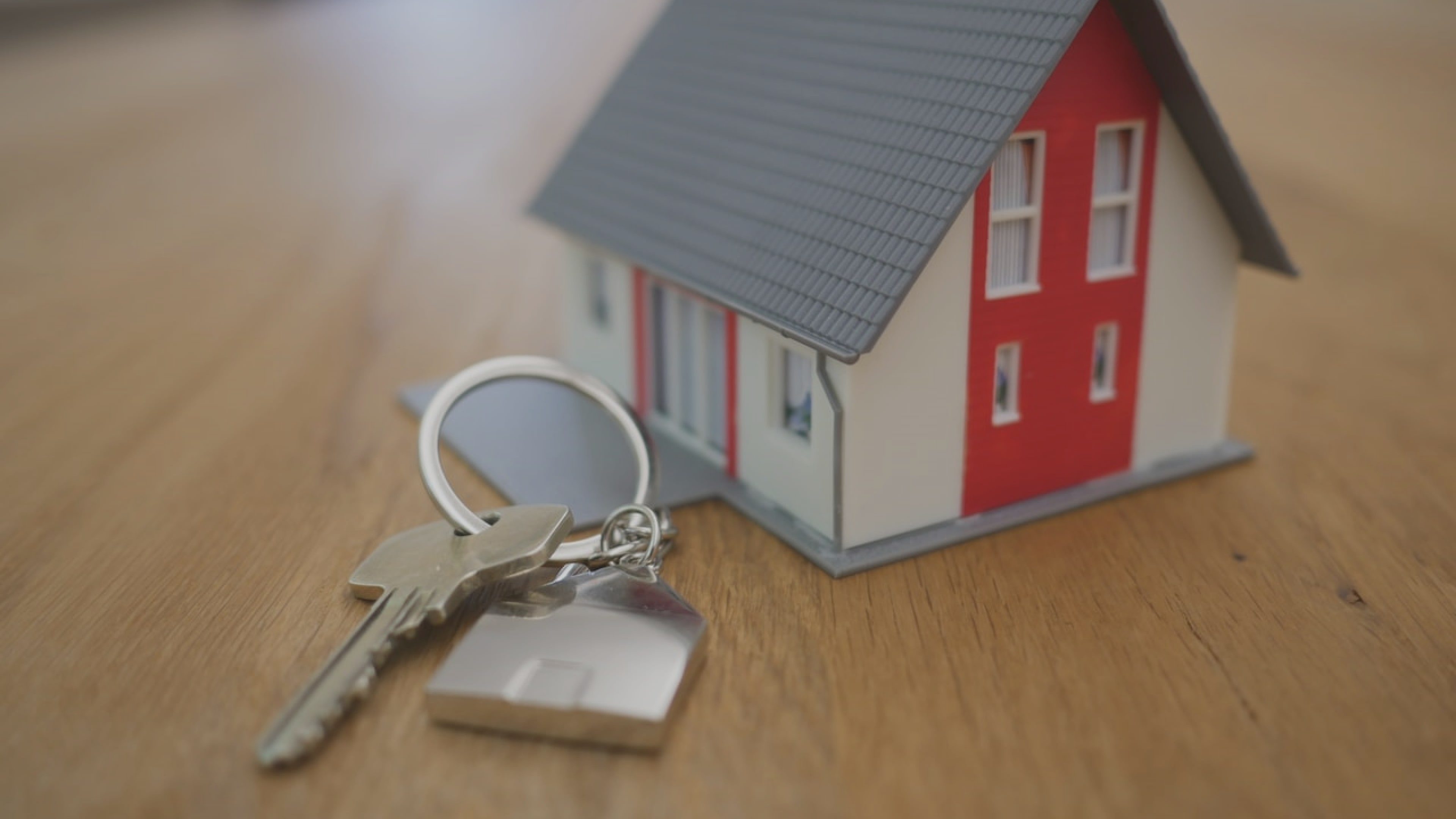 Miniature red and white house with a set of housekeys and keyring lying beside it on a wooden table