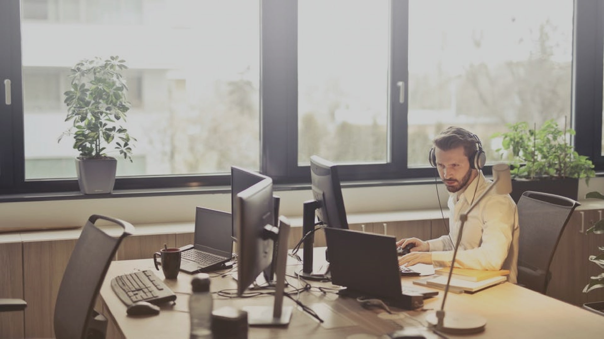 Man sitting at a desk in a communal office working on his computer and wearing headphones