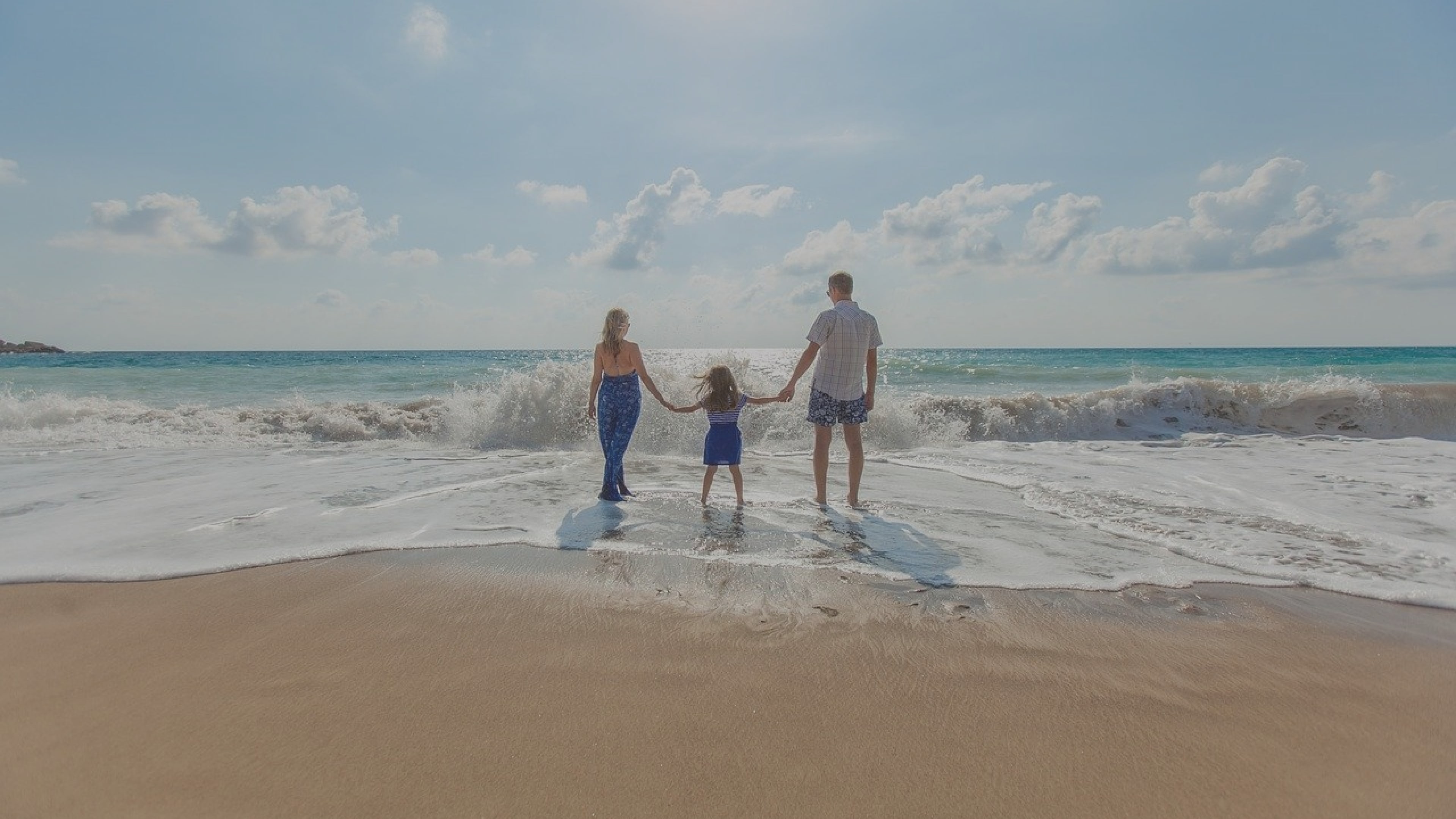 Couple on holidays standing in the sea and holding hands with their child